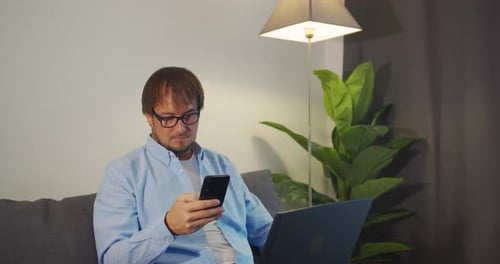 Man Using Cell Phone Sitting Indoors with Laptop