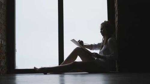 Silhouette of a Girl Artist Writing a Picture Near a Large Window
