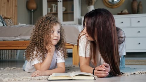 Lächelnde Mutter liest der Tochter im Vorschulalter auf dem Boden ein Märchen vor