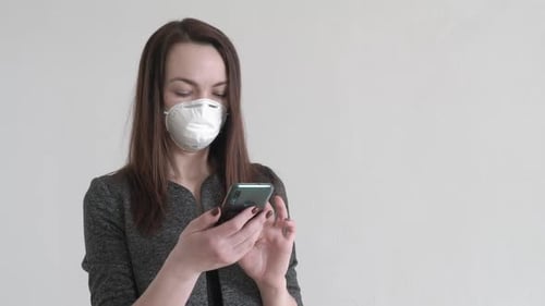 Portrait of Worried Woman Standing in Office in Protective Mask and Using Smartphone. Busy Young