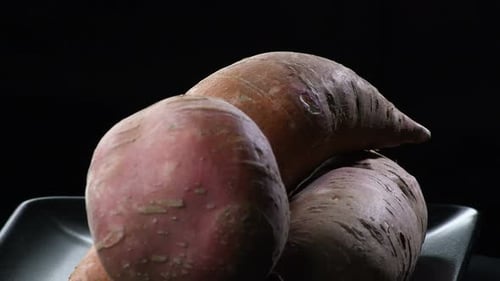 Three Raw Sweet Potatoes on a Dark Surface