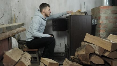 Man is throwing firewood log into wood oven. Heating house in village.