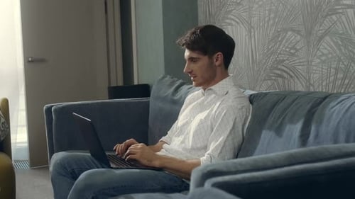Smiling Man Using Laptop in Hotel Room. Handsome Guy Chatting Computer Indoors.