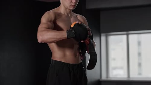 Fit Shirtless Man Putting on Boxer Gloves on His Hands in the Gym