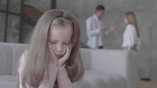 Petite fille triste assise sur le canapé au premier plan avec sa tête sur les mains