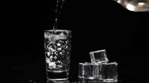 Schuss Wodka in Glas gießen. Schwarzer Hintergrund. Gießen Sie Alkohol ein Getränk