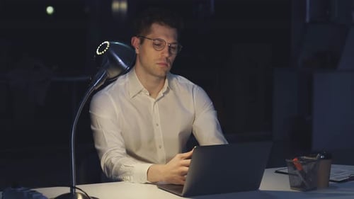 Jeune homme à lunettes travaille la nuit devant un ordinateur dans un bureau moderne