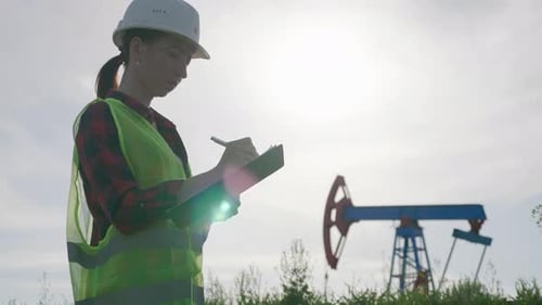 Ingenieurin schreibt auf Zwischenablage im Ölfeld. Frau trägt weißen Helm und Arbeitskleidung