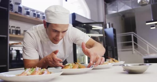 Mixed race male chef wearing chefs whites in a restaurant kitchen, putting food on a plate