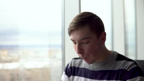 A Young Man Is Eating a Burger. A Man Sits in a Cafe By the Panoramic Window and Eats Fast Food.