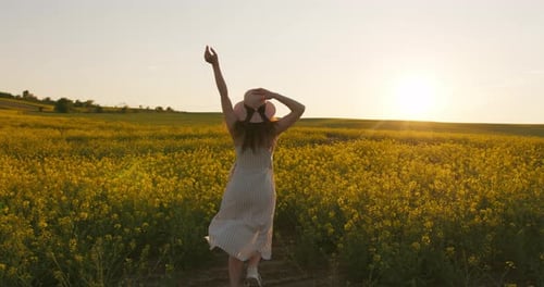 A Smiling Girl Is Running Across the Field and Holding Her Hat in Her Hands