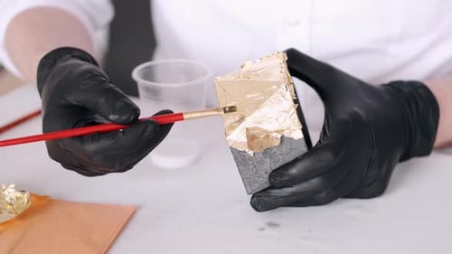 Nahaufnahme von Händen in Handschuhen mit Pinsel und Maltopf