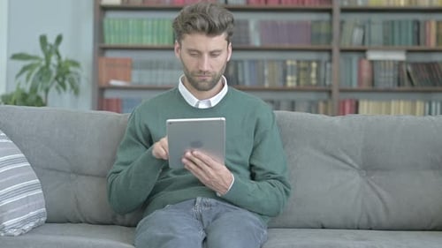 Man Using Tablet on Gray Couch at Home