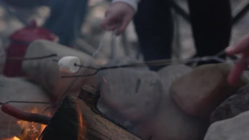 Panning down to campfire as marshmallows and hot dogs roast