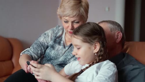 Grandparents and Grandchild Using Phone on Sofa Indoors