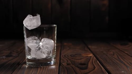 Close-up of Ice Cubes Falling Into an Empty Glass on a Dark Wooden Background.