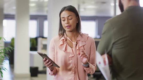 Video of diverse businesswoman and businessman using tablet and talking in office