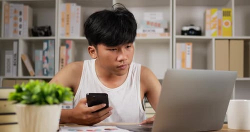 Young Adult Uses Phone and Laptop at Desk