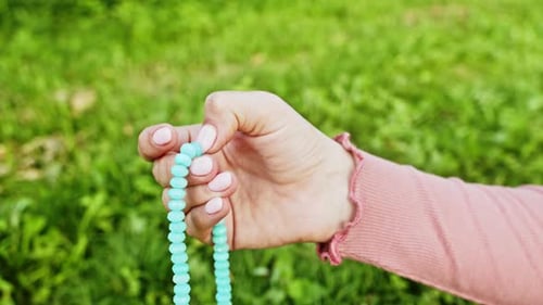 Hand der jungen gläubigen Frau betet in der Natur und verwendet handgefertigte Rosenkranzperlen, um Gebete zu zählen