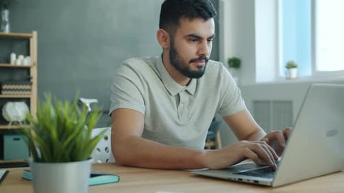Young Adult Man Typing on Laptop at Desk