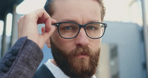Office Manager which Correcting His Glasses while Looking at Camera Outdoors Near Office Building