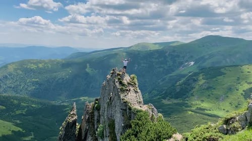 Man Standing on Mountain Peak with Arms Raised