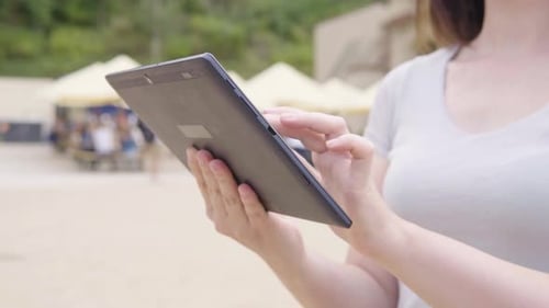 A Caucasian Woman Works on a Tablet in a City Park Closeup on the Hands and the Phone