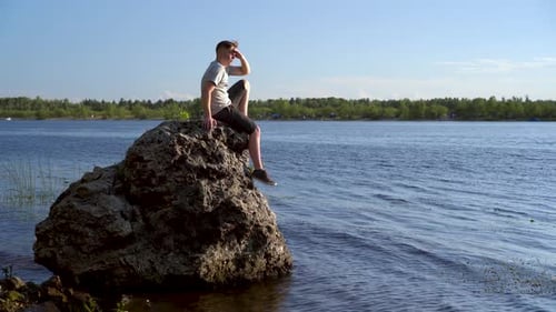 Ein junger Mann sitzt auf einem Stein am Fluss und bewundert die Natur. Ein Mann in der Natur.