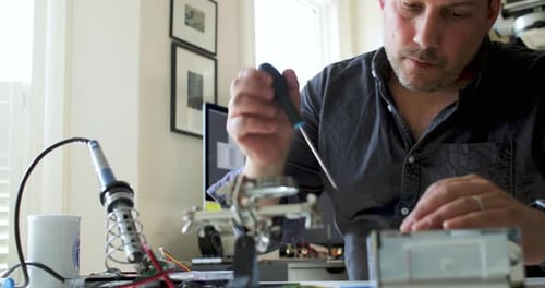 Man Repairs Electronics at Desk with Tools