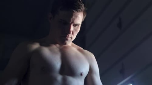 Still low angle shot of a shirtless MMA fighter in deep concentration in a moody setting with heavy