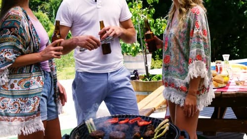 Group of friends having a bottle of beer while preparing barbeque