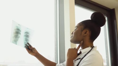 Eine afroamerikanische Ärztin oder Praktikantin untersucht eine Röntgenaufnahme der Lunge, die sie drinnen in den Händen hält