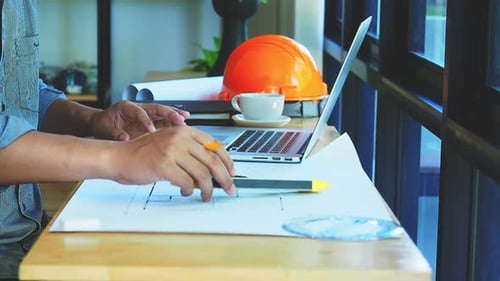 Architect is sitting in front of computer and arrange architectural equipment on desk.
