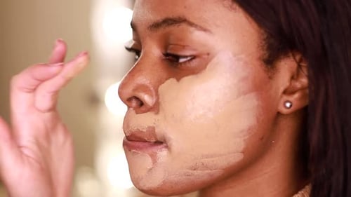 A female makeup artist applying gold makeup to a black African-American model.