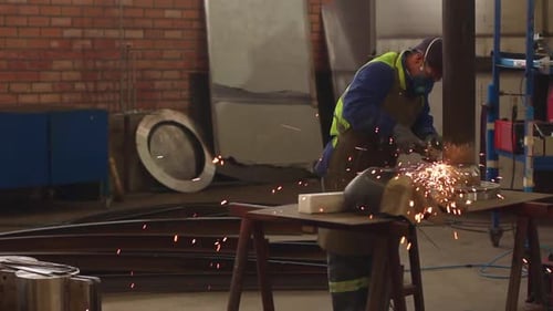 Arbeiter, der eine Schleifmaschine benutzt und Metall in einem Industriegebiet schneidet, mit Funkeneffekt.