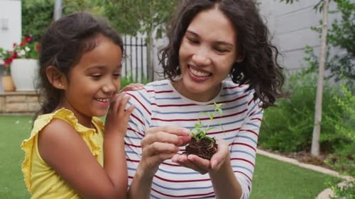 Hispanic mother and daughter teaching planting flowers in the garden