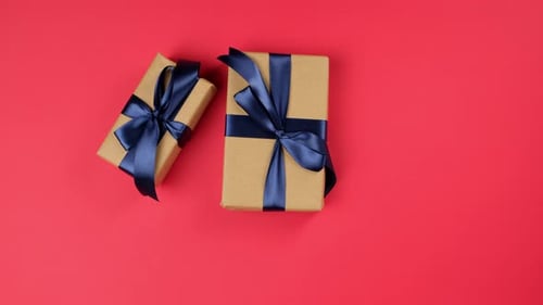 two female hands put two gift boxes with blue ribbon on a red surface, top view