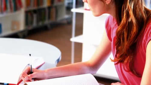 Aufmerksames Schulmädchen macht Hausaufgaben in der Bibliothek