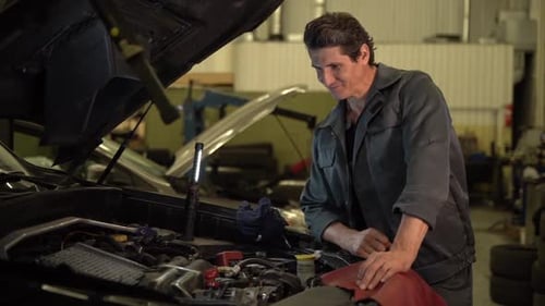 Im finish. Serious auto mechanic standing at the opened hood and looking inside car