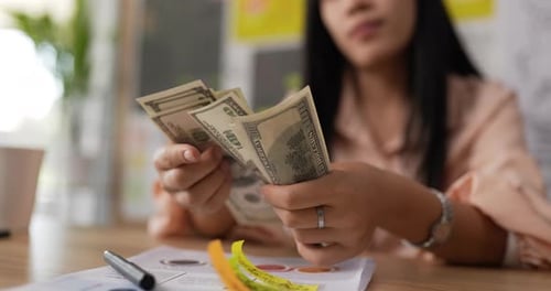 Woman Counts US Dollars at Desk