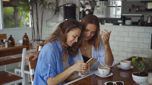 Two Woman Sharing Coffee Using Smartphone in Cafe in Slow Motion