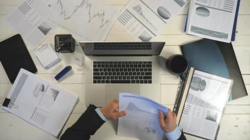 Top View Hands of Young Businessman Looking at Diagrams with Statistic on Paper and Typing Text on