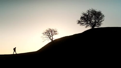 Man Silhouetted Against Sunset Walking Up Hill