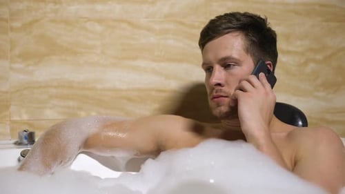 Un homme en colère se dispute avec sa petite amie sur un téléphone portable, prenant un bain de mousse relaxant