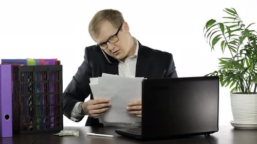 Businessman Working in Office. Talking Loudly on Telephone While Reading Papers