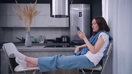 Woman Relaxing with Smartphone in Modern Kitchen