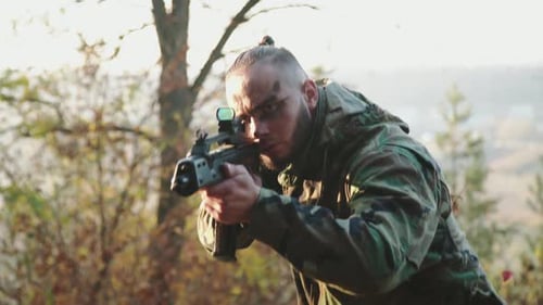 The Brutal Soldier Looks Into Laser Rifle Sight to Aims on the Object in Forest