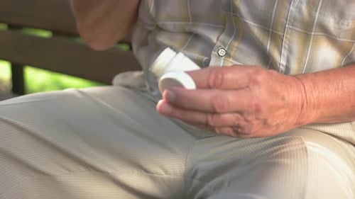 Senior Man Opens Medicine Bottle on Park Bench