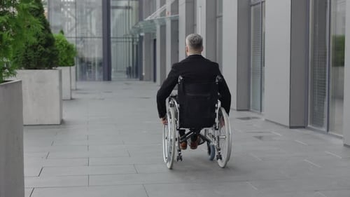Backside View of Male Person in Suit Moving While Sitting in Wheel Chair at Street