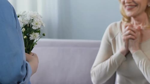 Child Presents Flowers to Happy Senior Woman